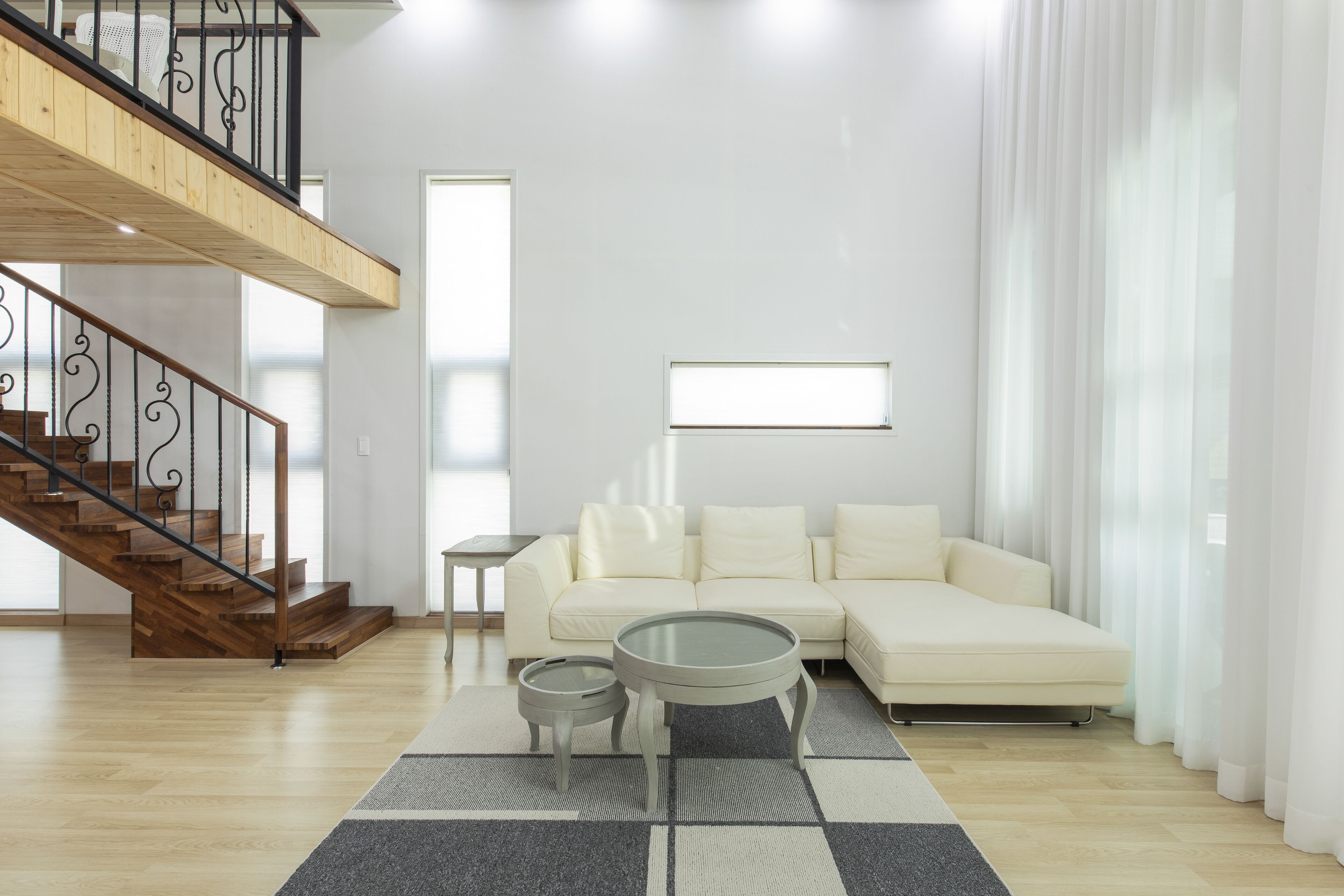 A modern living room with a wooden staircase, a white sofa, a glass coffee table, and a small side table.