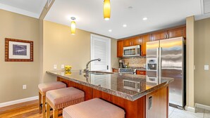 A kitchen with wooden cabinets, stainless steel appliances, a large island with stools, and a framed picture on the wall.