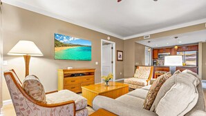 Una sala de estar con sofá, sillones, una mesa de centro, televisor y una zona de cocina con armarios y microondas.