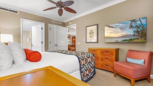 Habitación de hotel con cama, una silla, un armario de madera, un ventilador de techo y un cuadro de una playa.