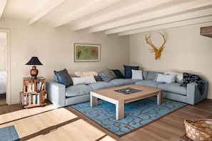 Uma sala de estar com sofá modular, mesa de centro, estante de livros, cabeça de veado na parede e tapete estampado.