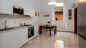 A modern kitchen with white cabinetry, a built-in oven, and a dining area with a wooden table and chairs. - SPANISH STEPS 3 BEDROOM PRESTIGIOUS HOME (Roma)