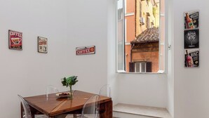 A dining area with a wooden table and clear chairs, a vase with flowers, and a window with a view of a building. - SPANISH STEPS 3 BEDROOM PRESTIGIOUS HOME (Roma)