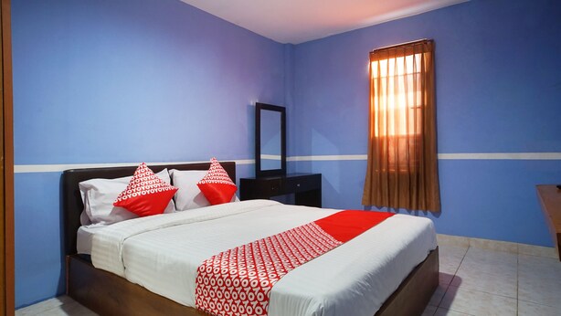 Een slaapkamer met een bed, nachtkastje, spiegel en raam met gordijnen.