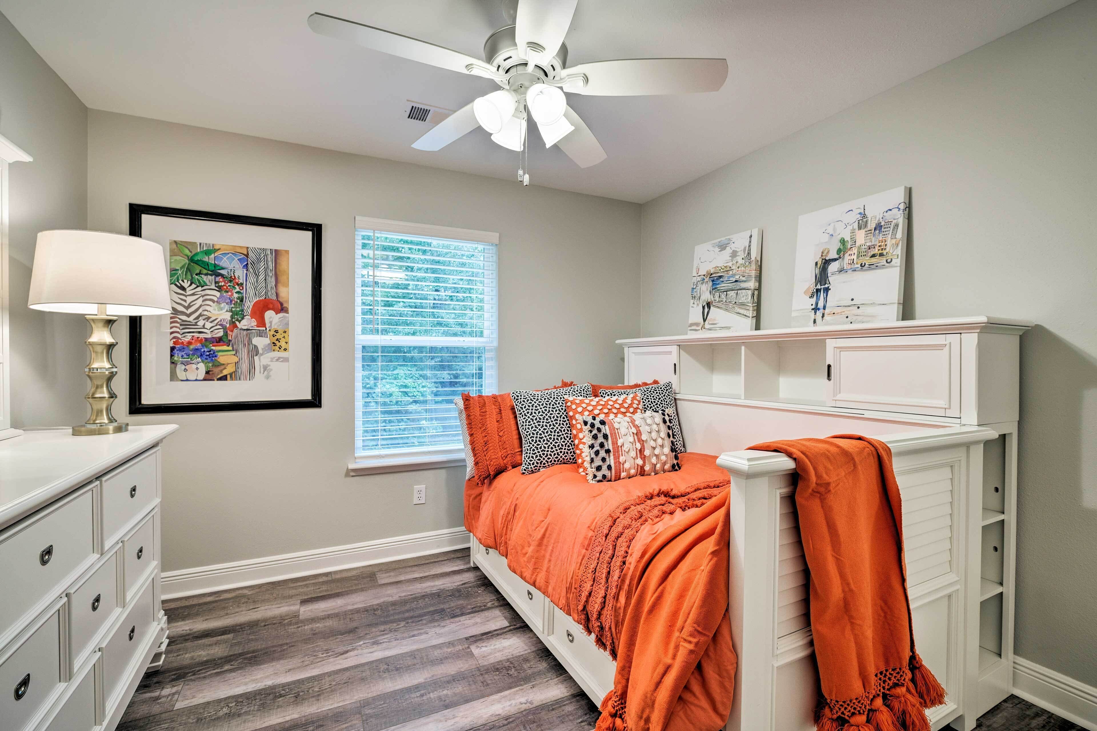 A bedroom with a bed, a ceiling fan, a window, and artwork on the walls.