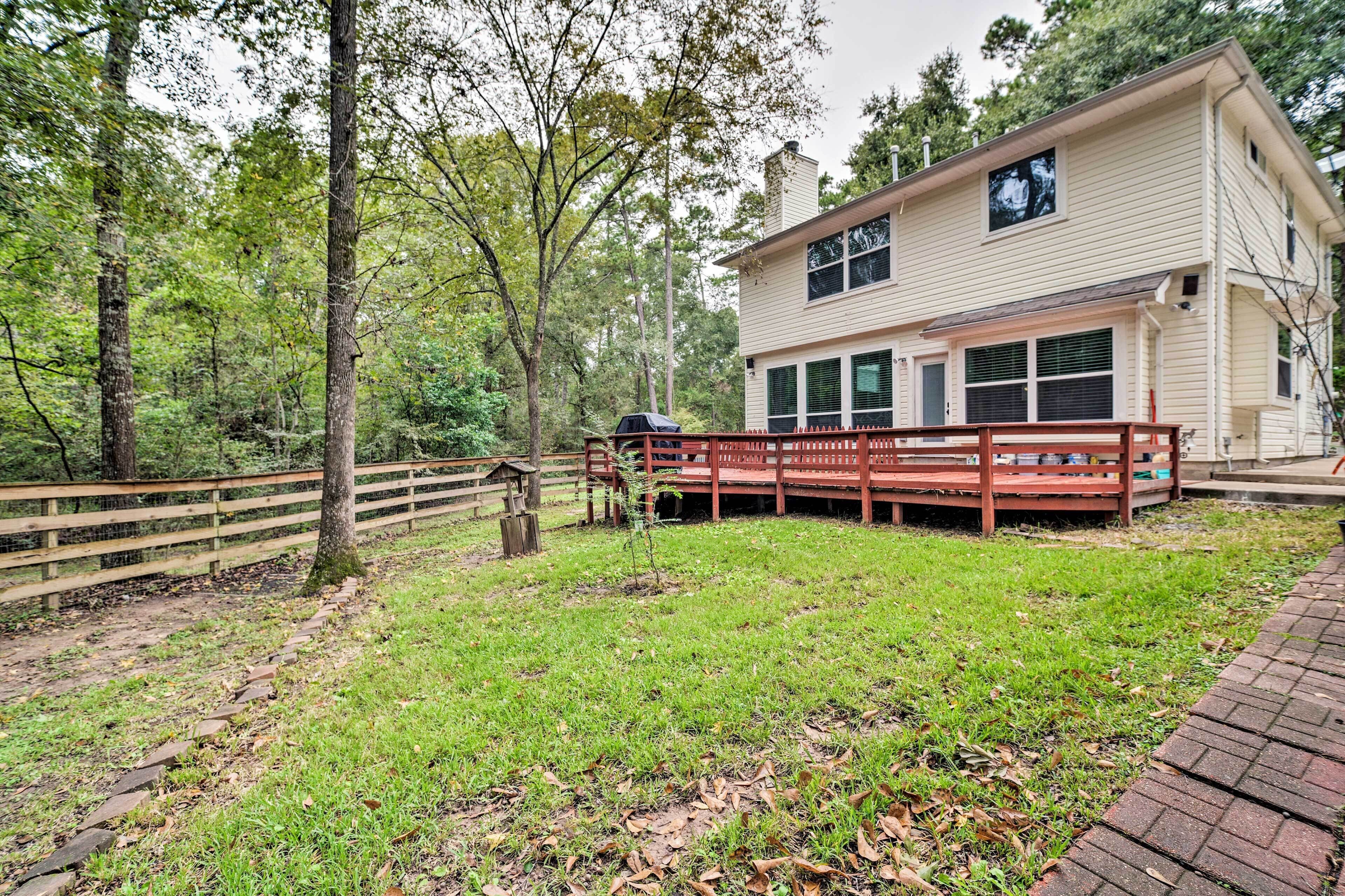 A two-story house with a deck, surrounded by a wooded area.