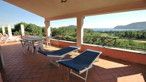 A covered outdoor area with two lounge chairs and a table, overlooking a scenic landscape with trees and hills.