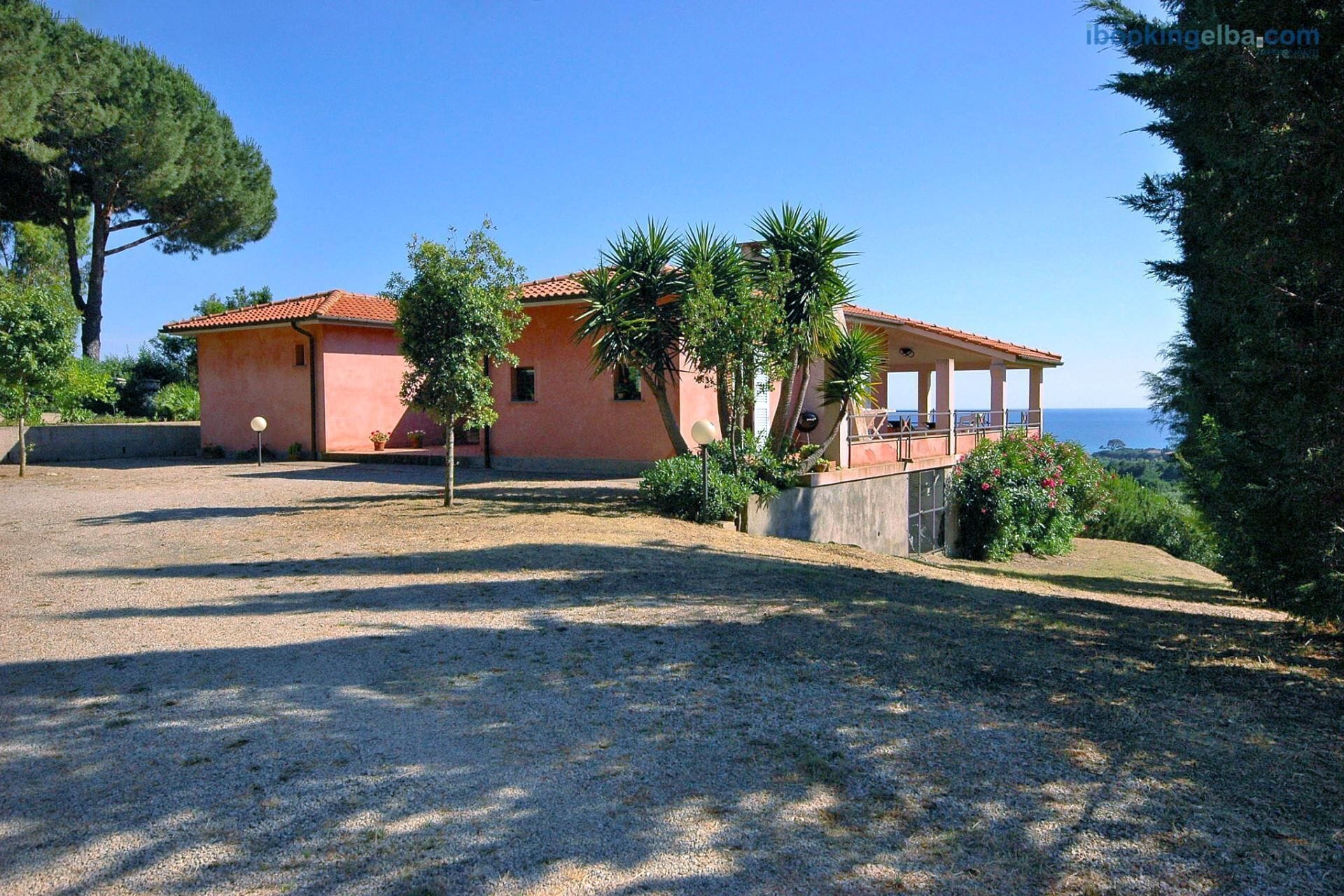 Eine pinkfarbene Villa mit überdachter Terrasse mit Blick aufs Meer.