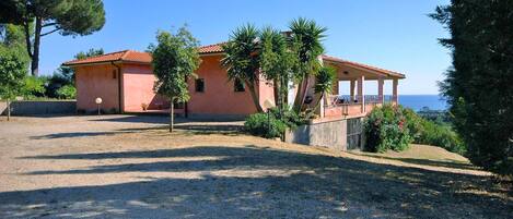 Eine pinkfarbene Villa mit überdachter Terrasse mit Blick aufs Meer.