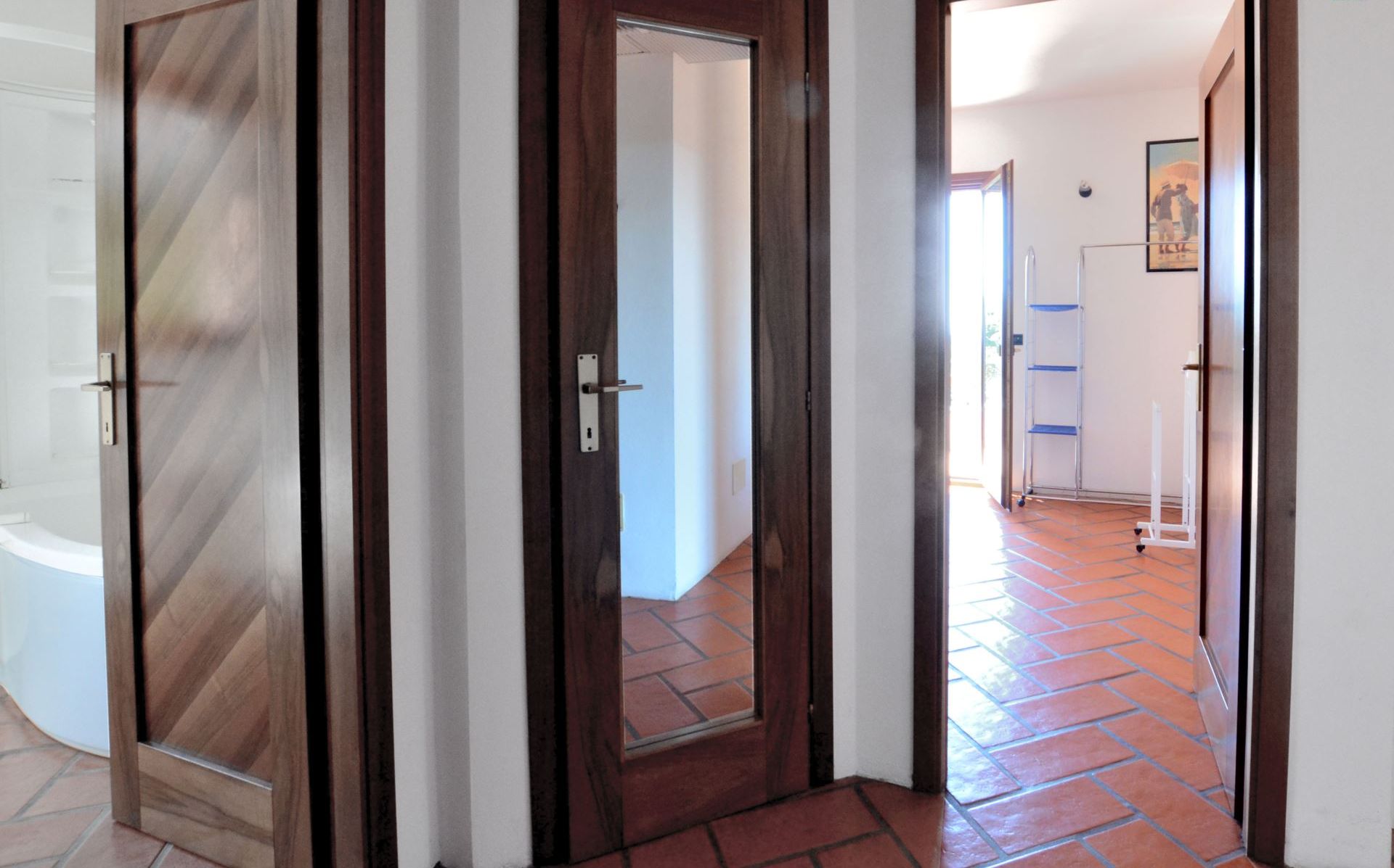 Un pasillo con puerta de madera y suelo de baldosas que conduce a un baño.