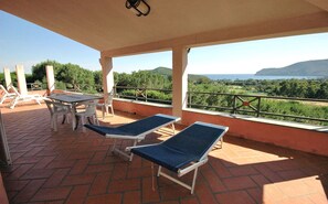 Un espacio exterior cubierto con dos sillones y una mesa, con vistas a un paisaje pintoresco con árboles y colinas.