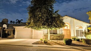 A residential house with a garage, a large tree in front, and a well-lit driveway at night. - Scottsdale Oasis! 5 BR, 7 beds, pool, 3000+ sq ft - near Mayo Clinic Hospital (Scottsdale)