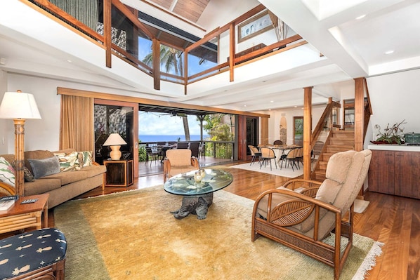 A spacious living area with a glass coffee table, wicker furniture, and a view of the ocean.
