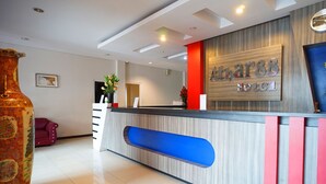 A hotel reception desk with a modern design, a large vase, and a red sofa in the background.