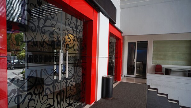 A hotel entrance with a red and white facade, a glass door with a logo, and a black trash bin.