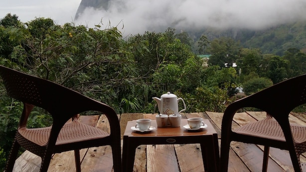 Una mesa de madera con una tetera, tazas y platos, dispuesta al aire libre.