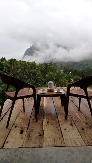 A wooden table with a teapot, cups, and saucers set outdoors. - Rawana Den (Ella)