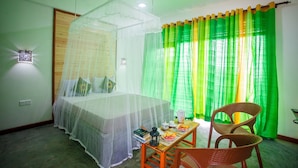 Una habitación con una cama bajo una mosquitera, una mesa con comida y libros, y una silla.
