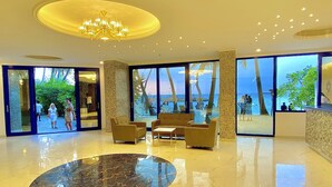 A spacious lobby with a marble floor, comfortable seating, large windows offering a view of the beach, and a chandelier. - Kaani Palm Beach (Maafushi)