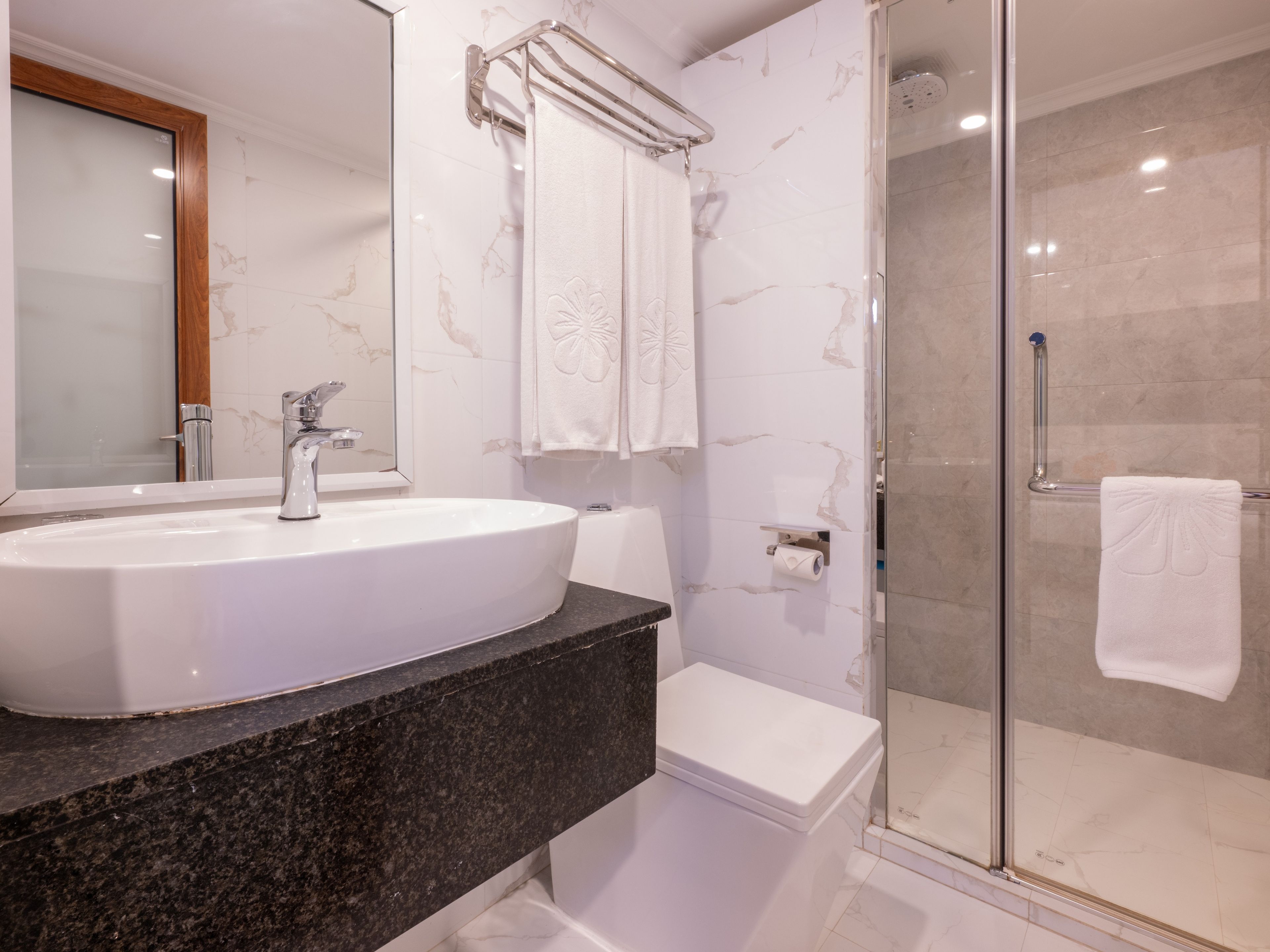 Un baño con lavamanos blanco, espejo, cabina de ducha con mampara de vidrio y un inodoro.