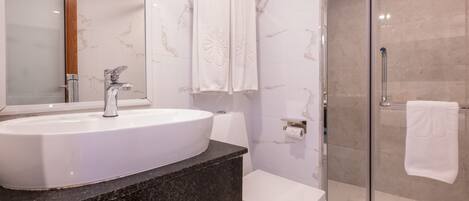 Un baño con lavamanos blanco, espejo, cabina de ducha con mampara de vidrio y un inodoro.