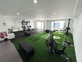 Un gimnasio con equipo de ejercicio, una bicicleta estática y una zona de césped artificial verde.