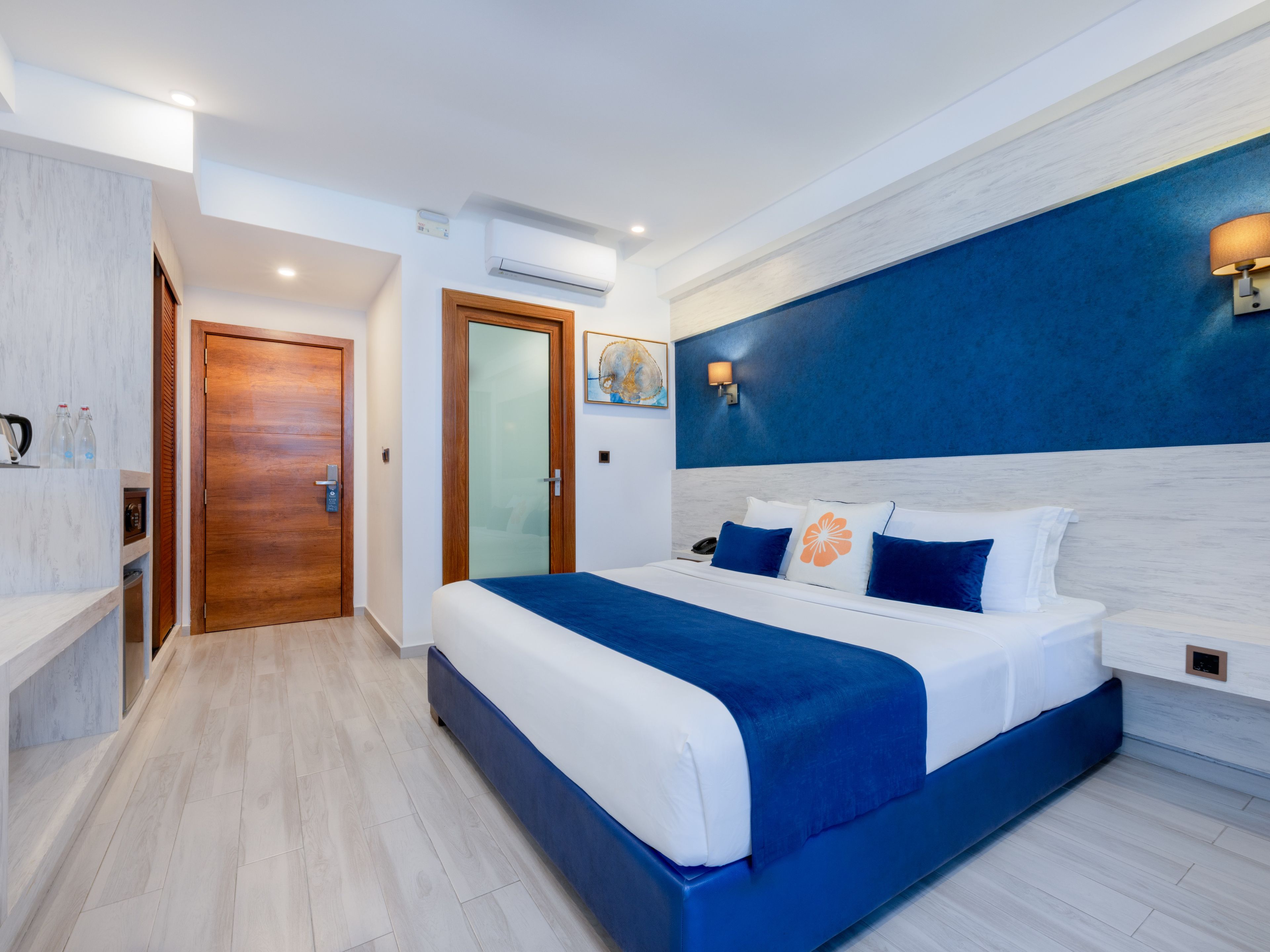 A modern hotel room with a large bed, a wooden door, and a blue accent wall.