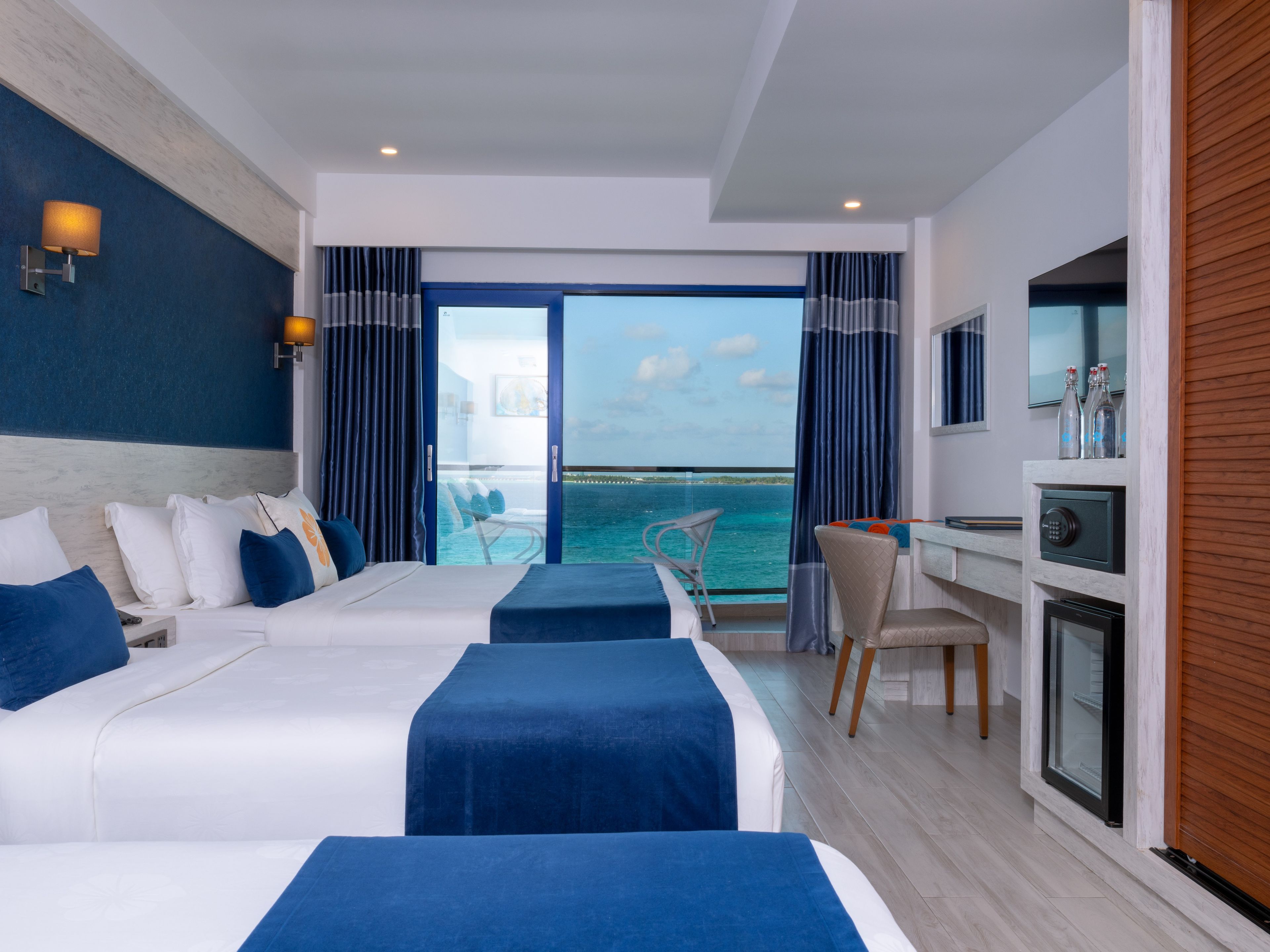 Habitación de hotel con dos camas, un escritorio, una silla, un televisor y vista al mar.