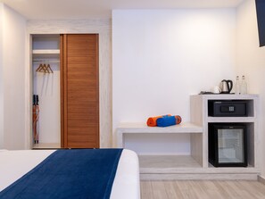 Habitación de hotel con cama, armario, una pequeña zona de estar, minibar y refrigerador.