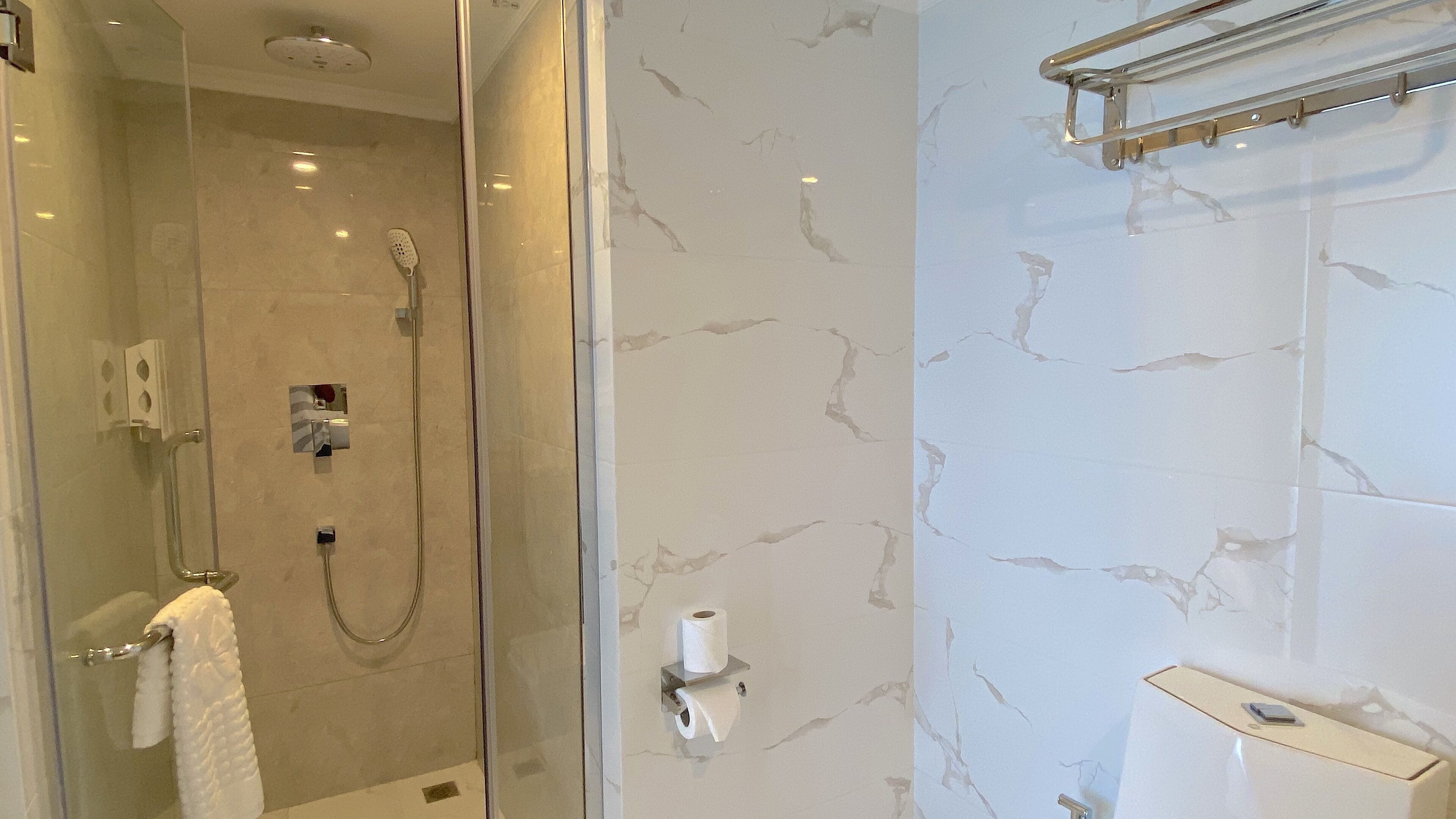 Un baño moderno con cabina de ducha de vidrio, paredes de mármol y un perchero para toallas.