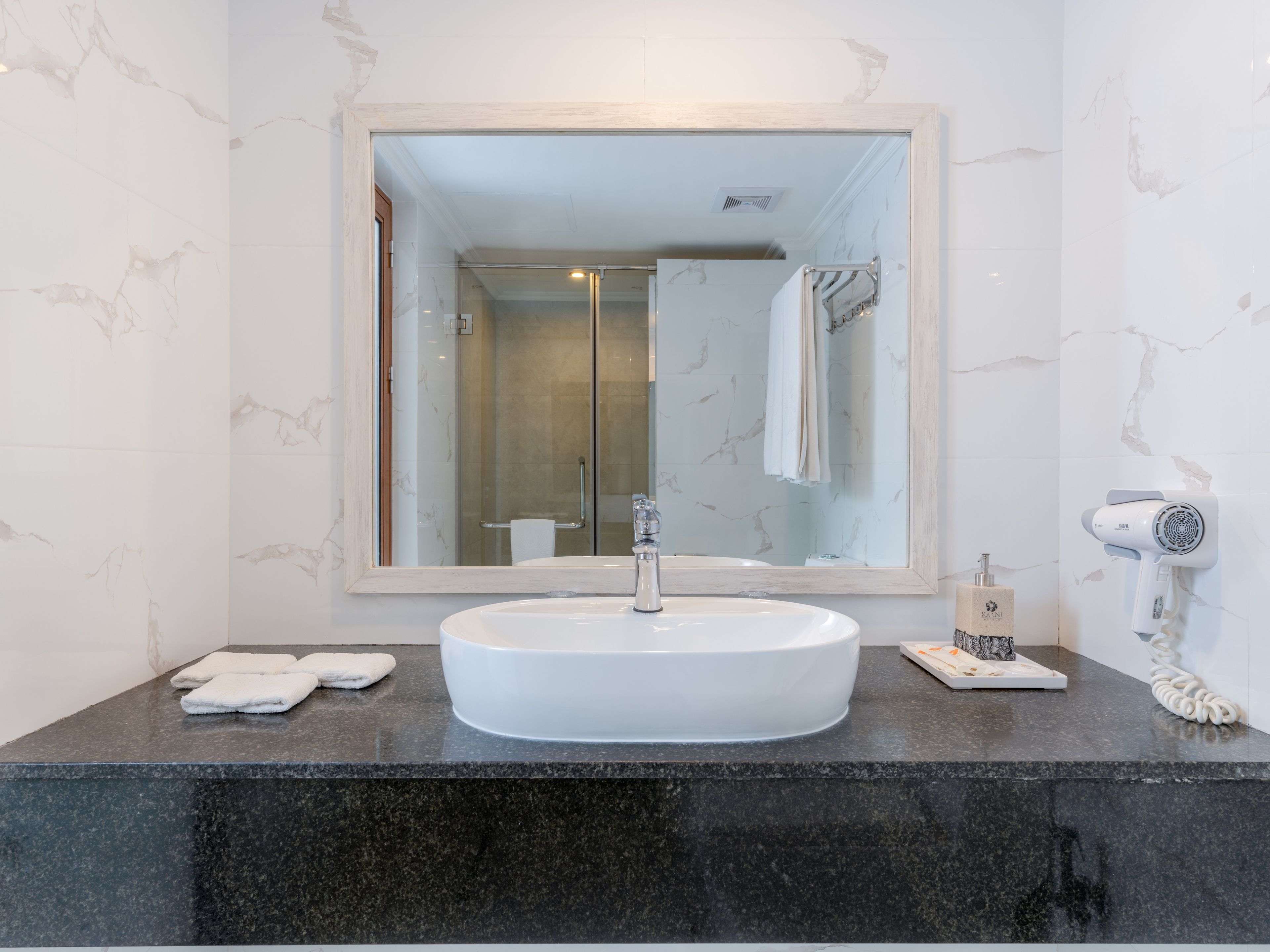 A bathroom with a large mirror, a white sink, a hairdryer, and a towel rack.