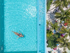 Una piscina con una persona flotando, rodeada de palmeras y sillas de playa.