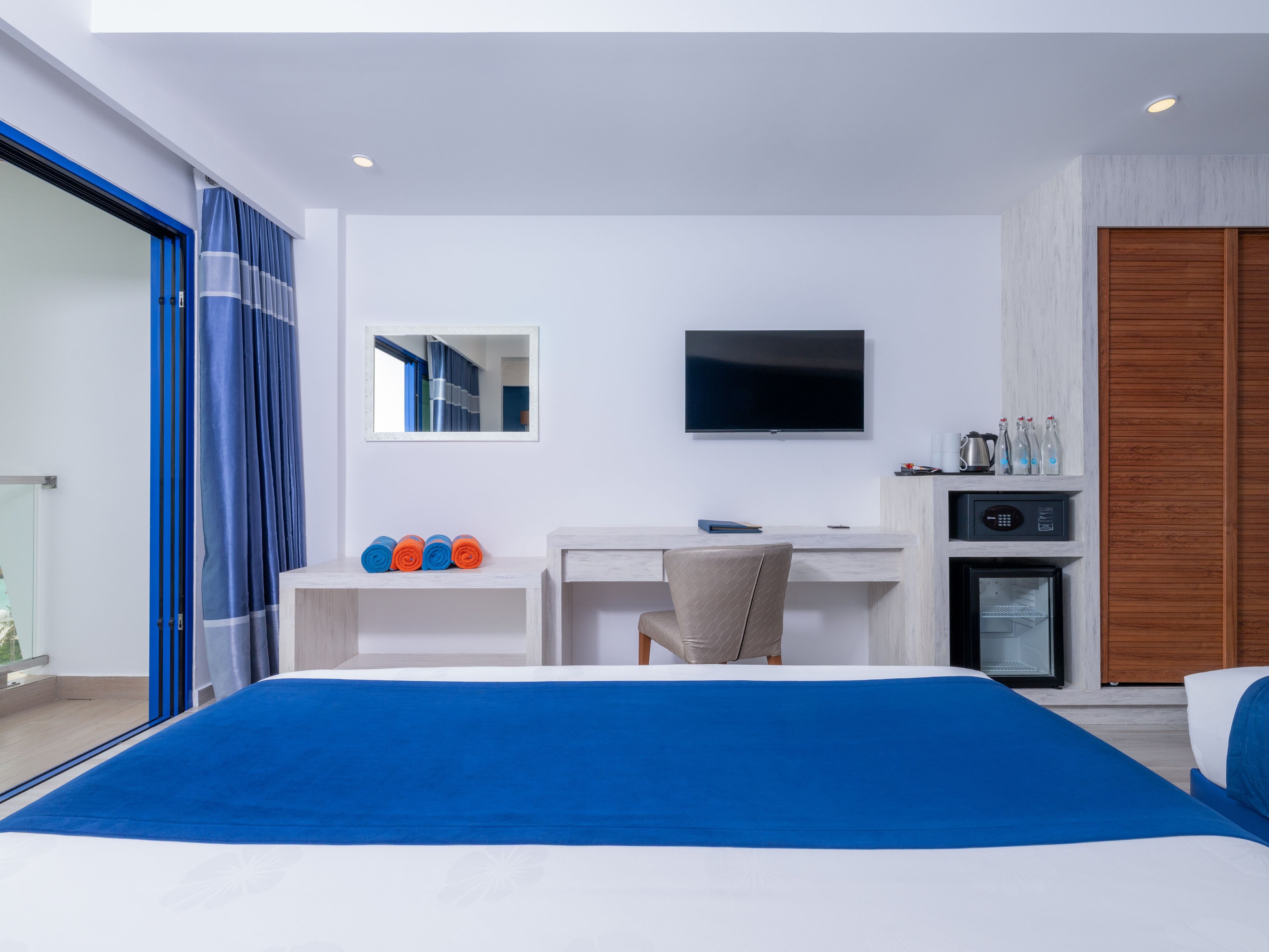 A hotel room with a bed, a desk, a television, and a minibar.
