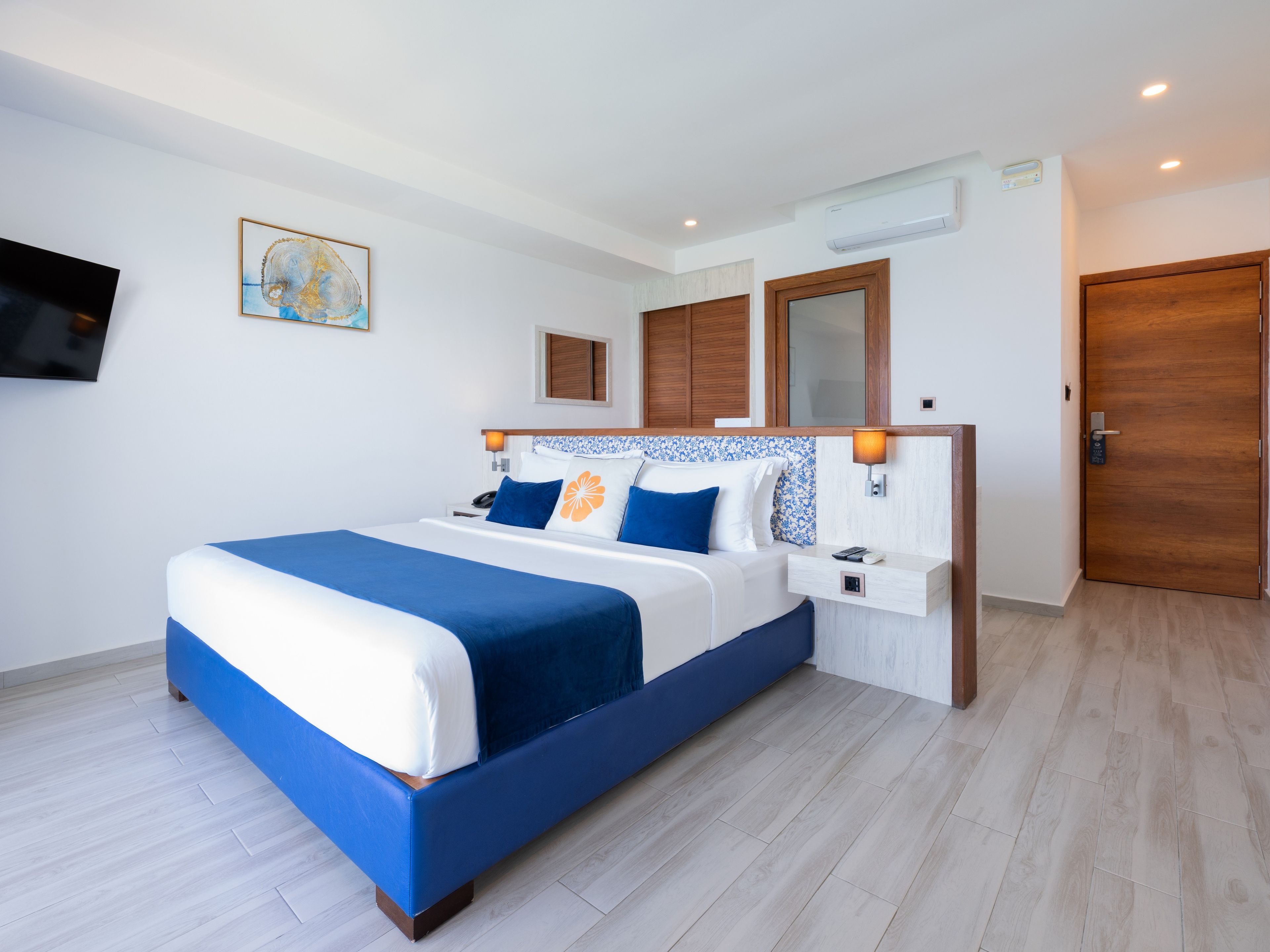 Ein modernes Hotelzimmer mit einem großen Bett, einem Nachttisch, einem an der Wand montierten Fernseher und einer Holztür.