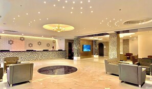 A spacious lobby with a reception desk, seating area, and a large screen. - Kaani Palm Beach (Maafushi)