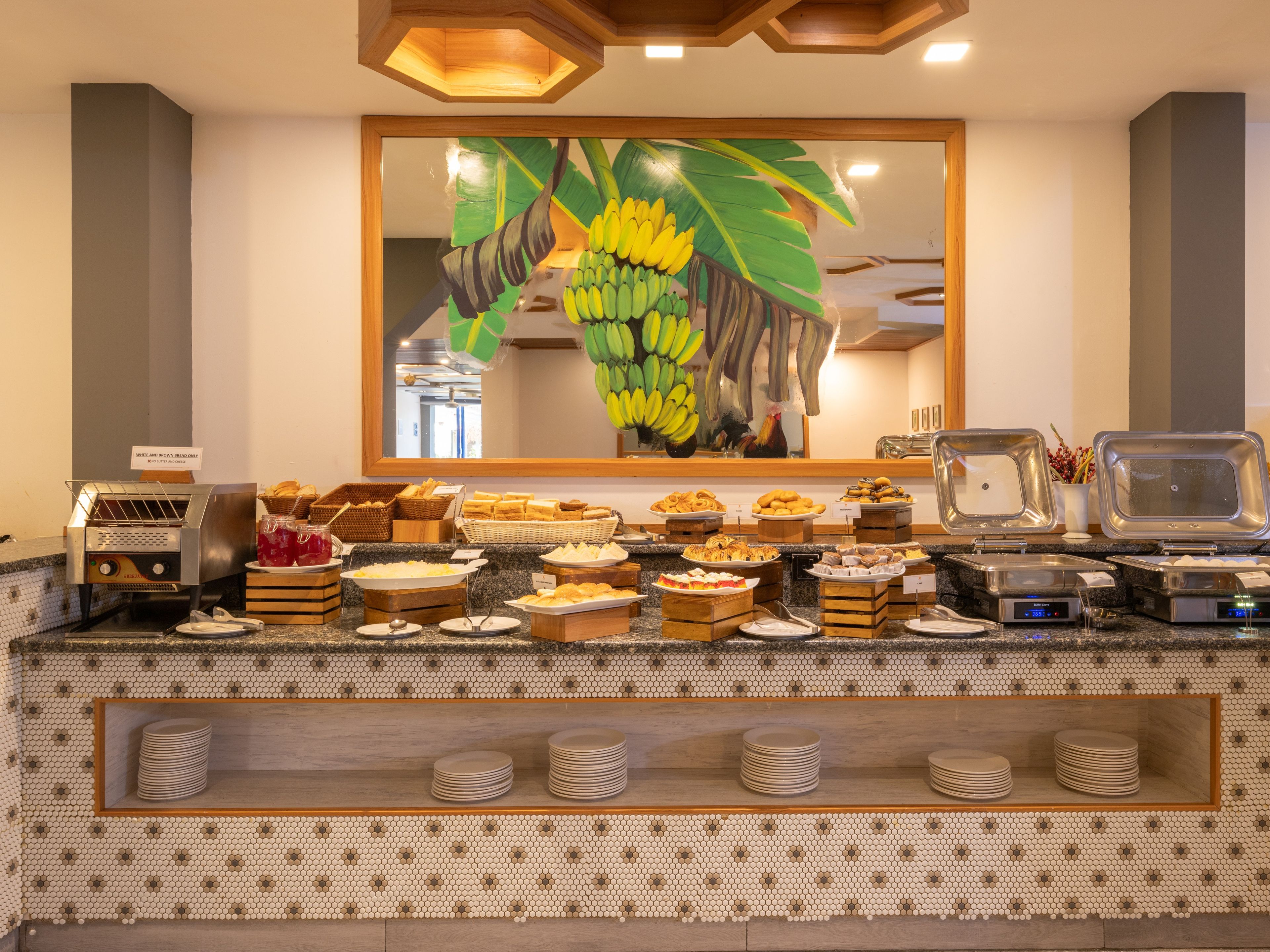 Un bufé con diversos alimentos y un tostador, dispuesto sobre una encimera con salpicadero de azulejos.