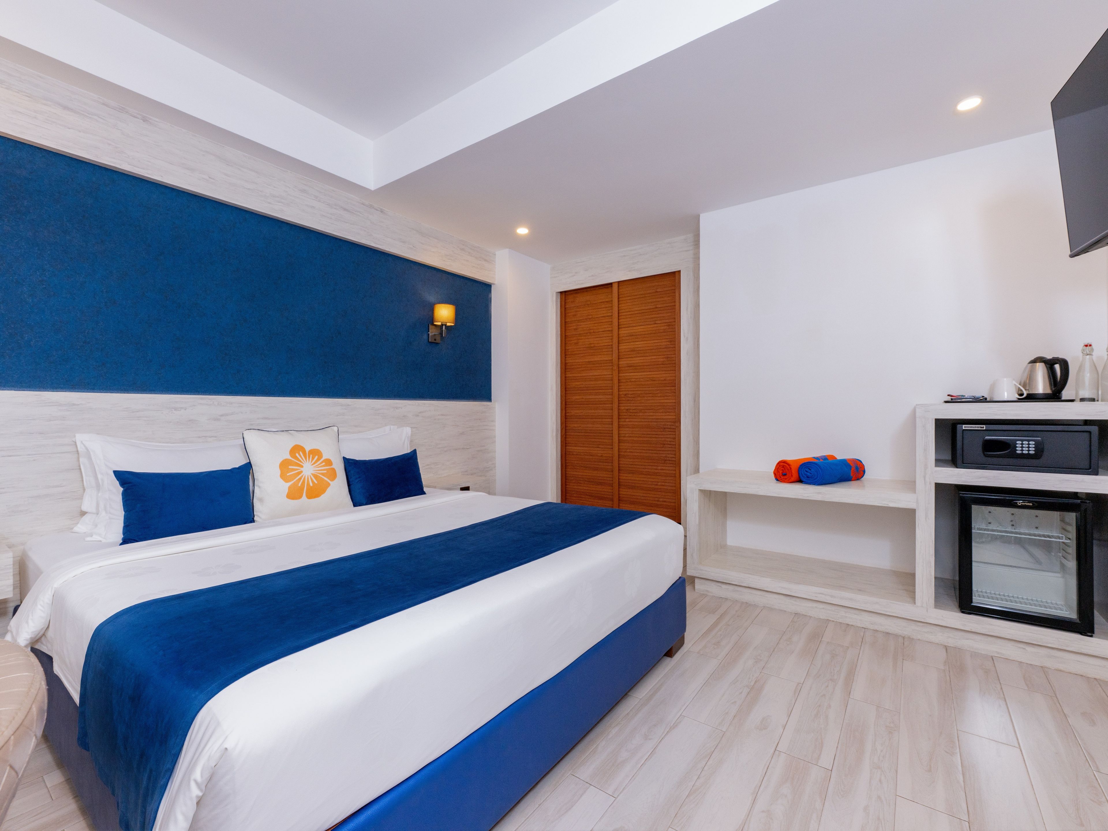 Une chambre d’hôtel moderne dotée d’un grand lit, d’un téléviseur intégré, d’un mini-réfrigérateur et d’une armoire en bois.