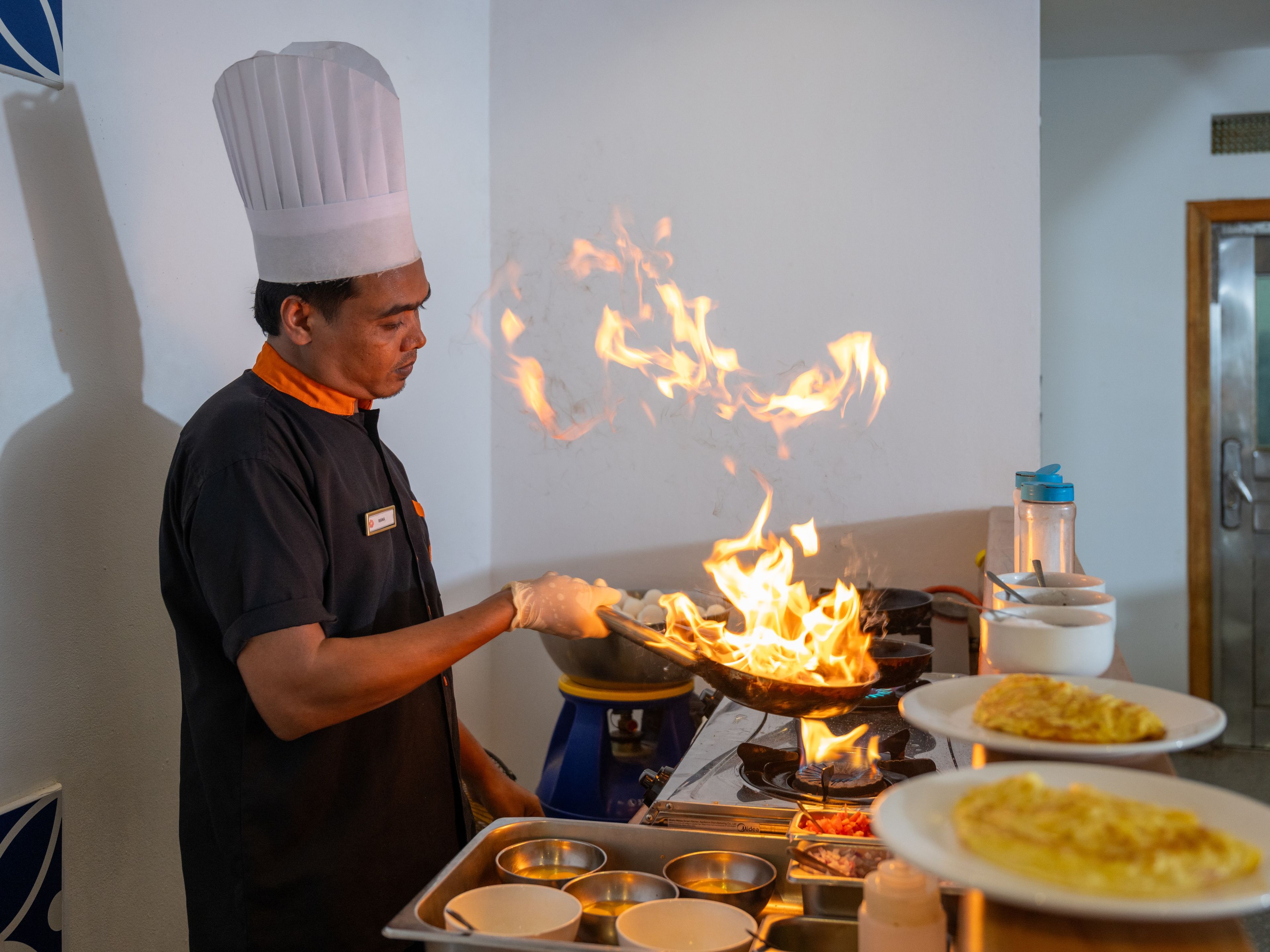 Un cocinero preparando comida en una sartén wok sobre una estufa con llamas.
