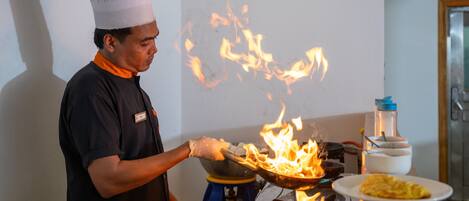 Un cocinero preparando comida en una sartén wok sobre una estufa con llamas.