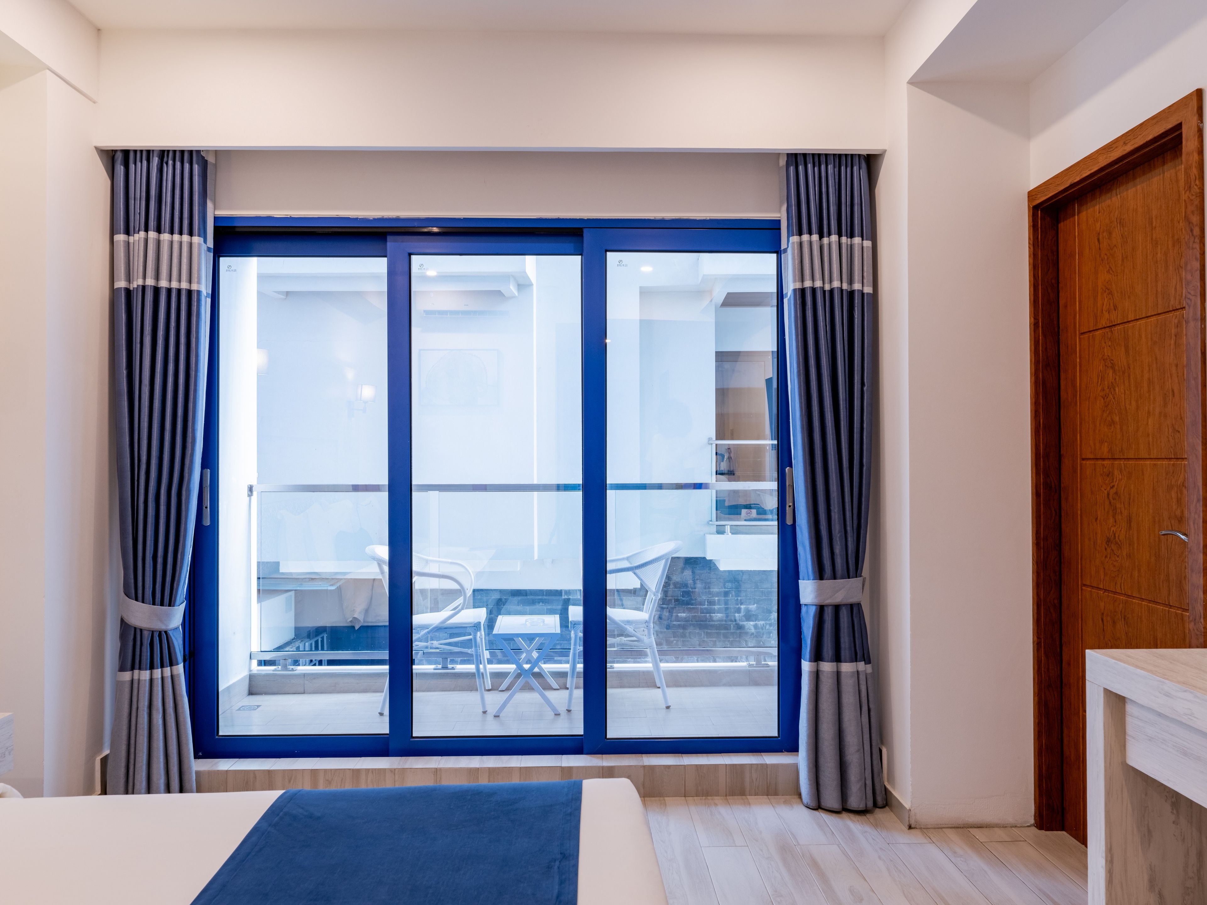 Une chambre d’hôtel dotée d’une grande porte-fenêtre coulissante donnant sur un balcon extérieur avec une table et des chaises.