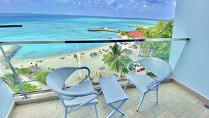 A balcony with two wicker chairs and a small table, overlooking a beach with clear turquoise waters and a distant island. - Kaani Palm Beach (Maafushi)