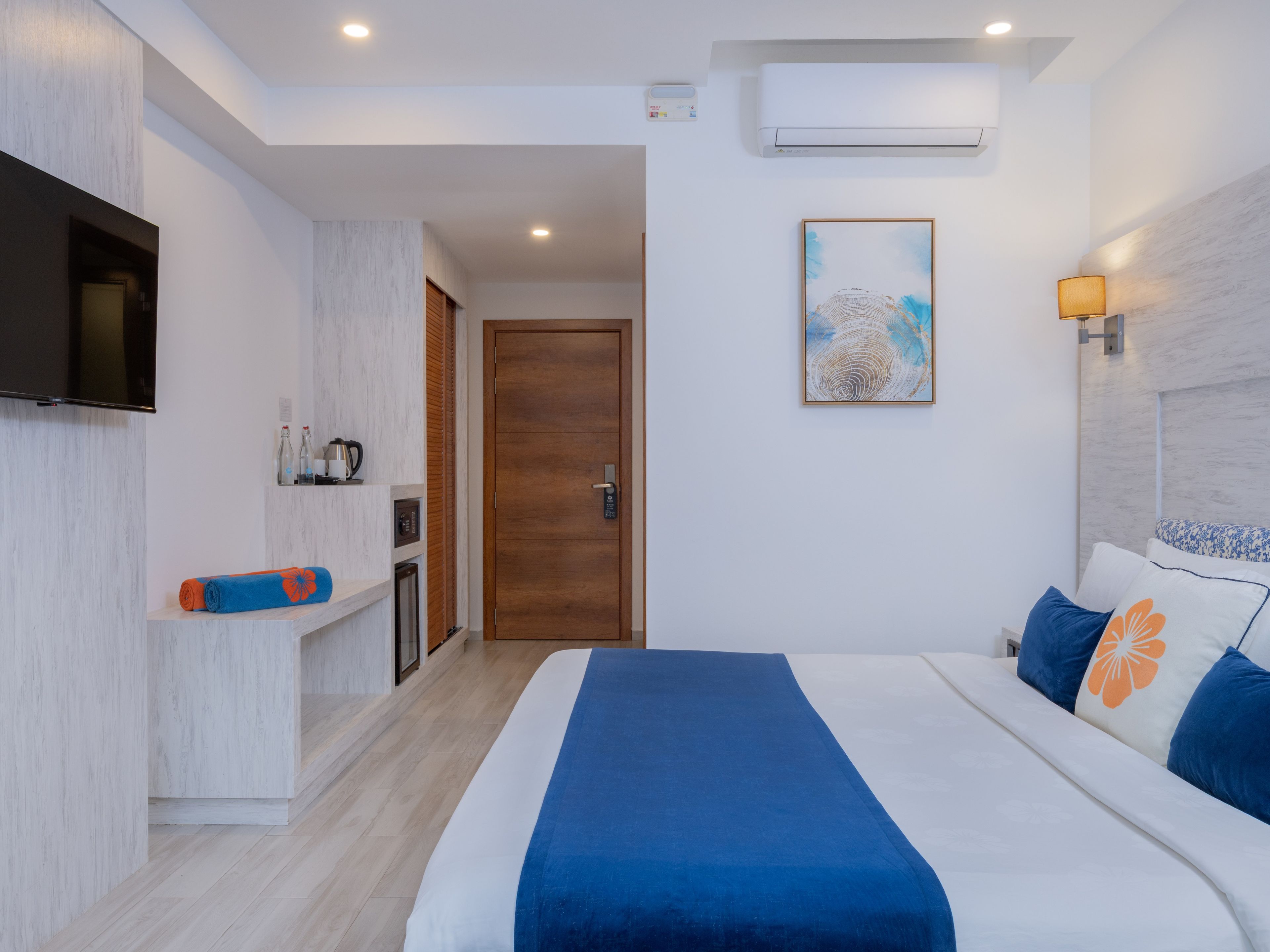 Habitación de hotel con cama, televisor, aire acondicionado instalado en la pared y puerta que da a un baño.