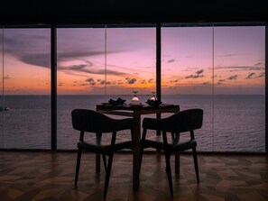 A dining area with a table and chairs facing a large window overlooking the sea. - Kaani Palm Beach (Maafushi)