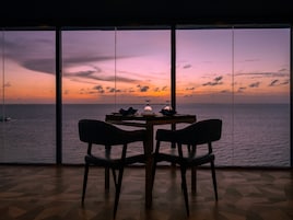 Comedor con mesa y sillas frente a un ventanal con vistas al mar.
