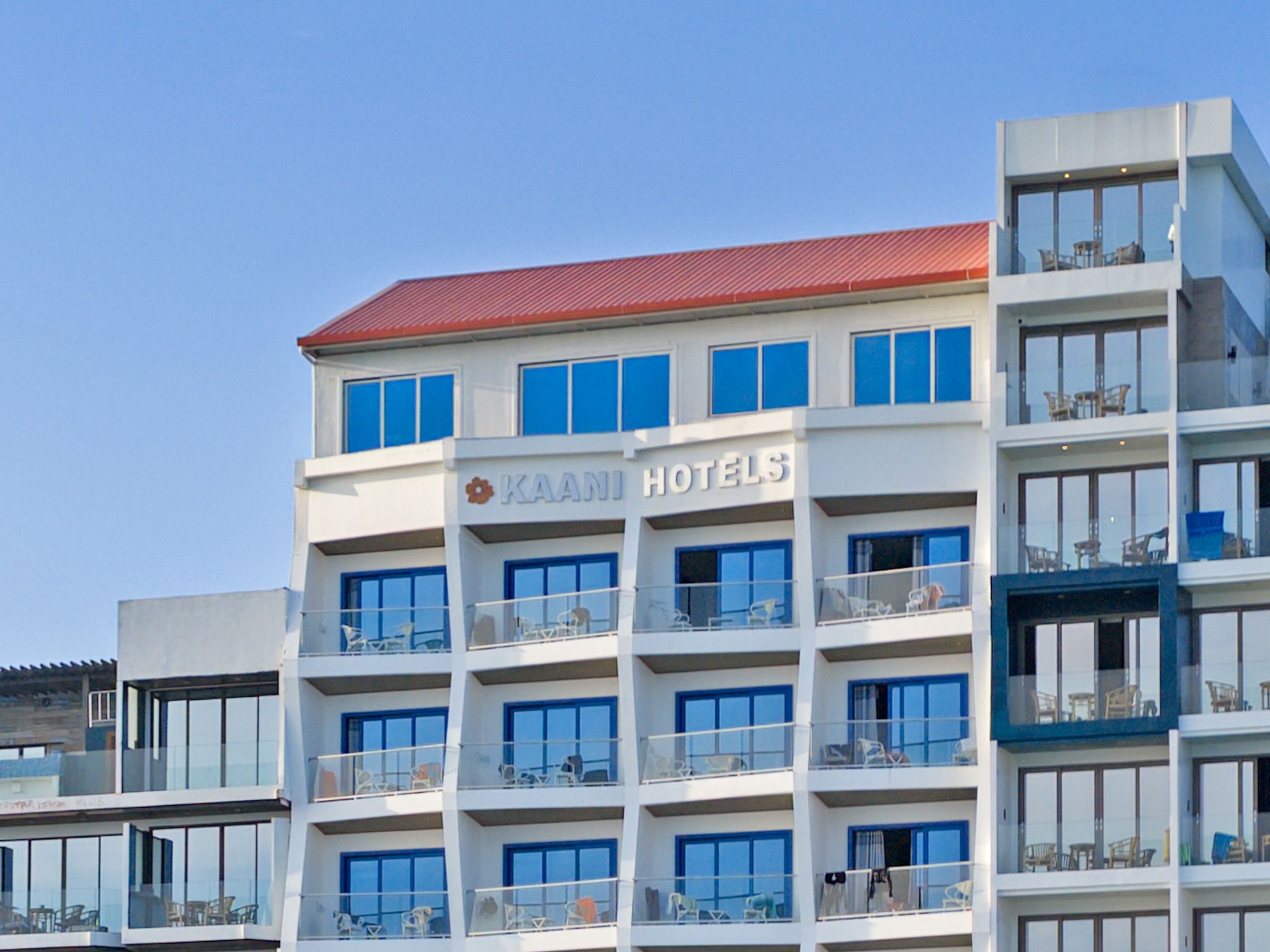 A multi-story hotel building with balconies, a red roof, and the name 'KAANI HOTELS' displayed on the facade.