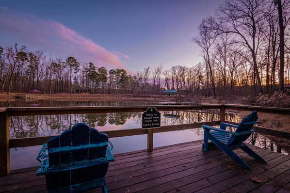 A wooden deck with two Adirondack chairs, a sign indicating fishing for tranquil shores is for guests only, and a sunset view over a body of water.