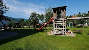 A playground with a slide and climbing structure, surrounded by grass and trees.