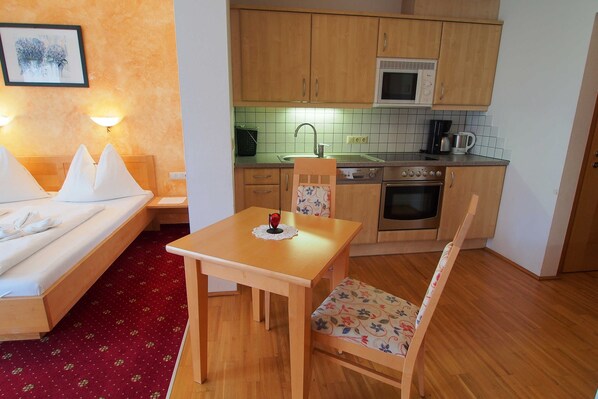 A hotel room with a bed, a small table with a chair, a kitchenette with a microwave, a coffee maker, and a sink.
