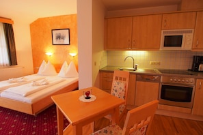 A hotel room with a bed, a small table with a red rose, a microwave, a sink, and a stove.