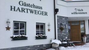 En byggnad med skylten ”Gästehaus HARTWEGER” och en välkomnande skylt med texten ”Willkommen”.